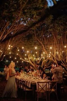 a group of people sitting around a table with lights hanging from the trees over them