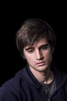 a young man is posing for a photo in front of a black background and wearing a hoodie