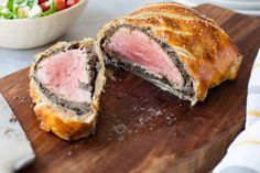 a meatloaf roll cut in half on a wooden cutting board next to a salad