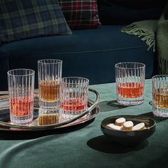 several glasses with different colored liquids sit on a table next to a plate full of marshmallows