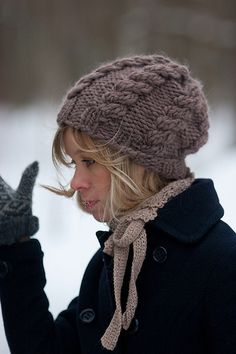 a woman wearing a knitted hat and scarf holds her hand up in the air