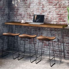 three stools and a table in front of a brick wall with a laptop on it