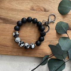 a black and white beaded bracelet sitting on top of a wooden board next to leaves