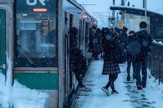 people are walking on the snow covered platform next to a train