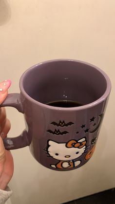 a woman holding a purple hello kitty coffee mug in her right hand with bats on it