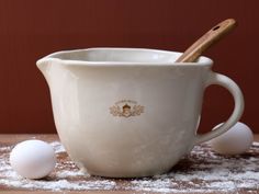 a white cup sitting on top of a wooden table next to three eggs and a cinnamon stick