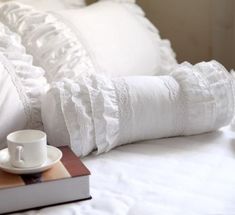 a book, cup and saucer on a bed with white ruffles in the background