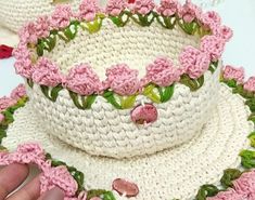 a crocheted hat with pink flowers on it is being held by someone's hand