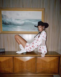 a woman sitting on top of a dresser in front of a painting and wearing white boots