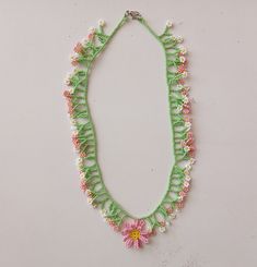 a green and pink beaded necklace with flowers hanging from it's side on a white surface