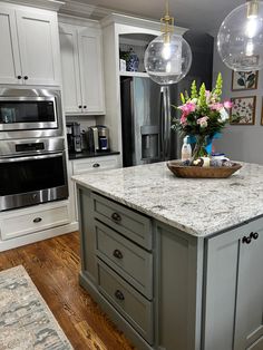 a kitchen island with marble counter tops and two hanging lights above it, surrounded by white cabinets