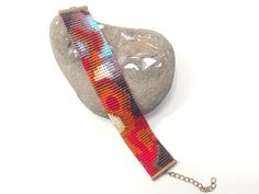 a beaded bracelet on a rock with a chain attached to the clasp, sitting next to a rock