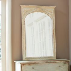 a white dresser with a mirror on top of it next to a window in a room