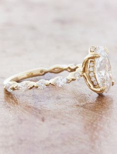 a yellow gold engagement ring with an oval cut diamond surrounded by small white diamonds on a wooden surface