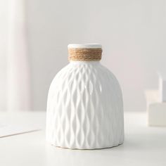 a white vase with a rope wrapped around the top on a table next to some books