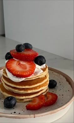 a stack of pancakes with strawberries and blueberries on top