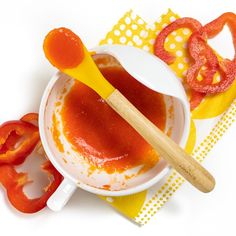 a white bowl filled with sauce next to sliced tomatoes and a wooden utensil