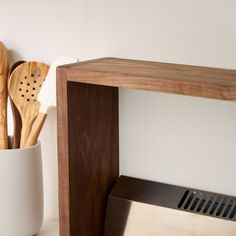 utensils in a white vase next to a wooden shelf