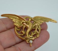 This is a very versatile piece. It can be adorned as a pendant, a brooch as well as a watch pin. It originates from France and is hallmarked with the French eagles head guarantying that it is 18K solid gold. This incredibly detailed puce dates from the 1890s-1910 (Art Nouveau Era). It is a rendering of a winged chimera (dragon or griffin). The griffin is in flight with a single round pearl braced in its mouth. This dragon has a wing span of 2.5 inches so it is not a tiny piece. The back of the p Art Nouveau Brooch, Art Nouveau Gold Brooch With Cabochon, Gold Locket Brooch For Collectors, Unique Gold Brooch With Cabochon, Unique Gold Brooches With Cabochon, Unique Gold Pendant Brooches, Heirloom Pendant Brooches As Gifts, French Art Nouveau, Art Nouveau Pendant