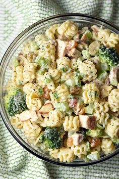 a glass bowl filled with pasta salad on top of a green and white table cloth