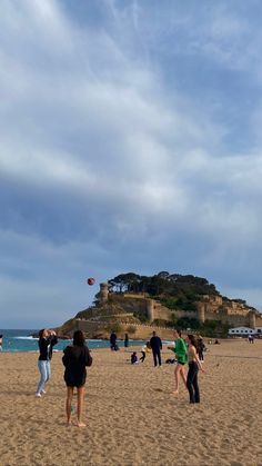 people are on the beach flying kites in the sky near an old castle like structure