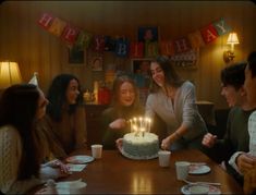 a group of people sitting around a table with a birthday cake on top of it