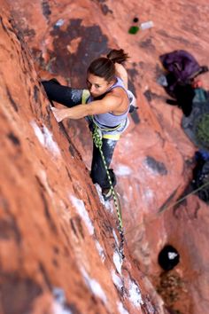 a woman climbing up the side of a red rock with her hands on her hips