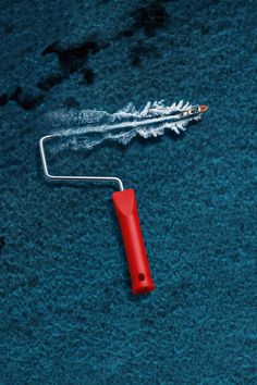 a red paint roller laying on top of a blue carpet next to a white brush