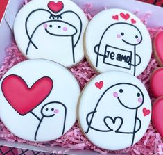 four decorated cookies in a box with pink sprinkles and hearts on them