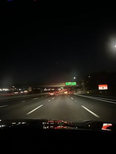 a car driving down a highway at night with lights on and street signs in the distance