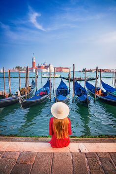 a woman sitting on the edge of a pier looking at gondolas