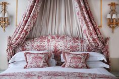 the canopy bed is made up with red and white sheets, pillows, and throw pillows