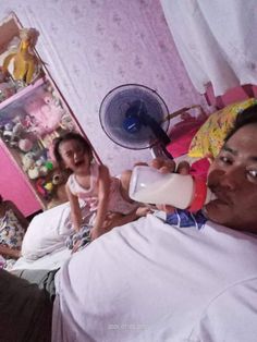 a man drinking milk from a glass while sitting on a bed with two other people in the background