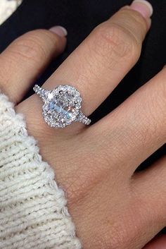 a woman's hand with a diamond ring on top of her finger and a white sweater