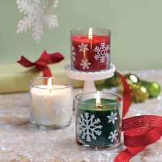 three candles with snowflakes on them sitting in front of christmas decorations and presents