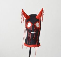 a knitted mask with red eyes and horns on top of a wooden stick in front of a white wall