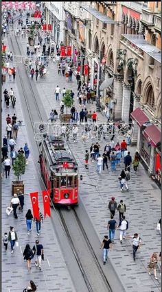 a red trolley car traveling down a street next to lots of people on the sidewalk