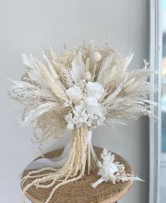 a vase filled with white flowers and feathers on top of a wooden table next to a window