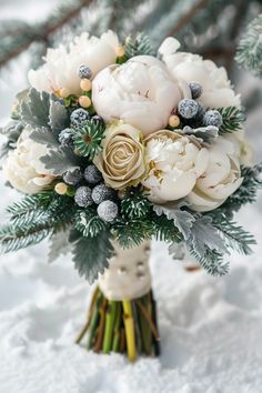 a bridal bouquet with white flowers and greenery in the snow on a snowy day