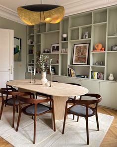 a dining room table with chairs and a vase on it in front of bookshelves