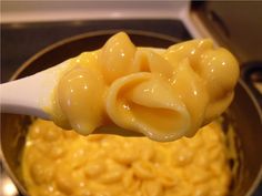 a spoon full of macaroni and cheese is being held over the stove top