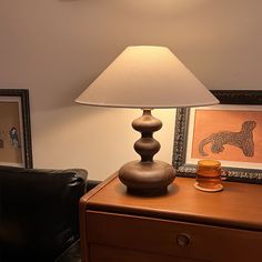 a lamp sitting on top of a wooden table next to a black chair and framed pictures