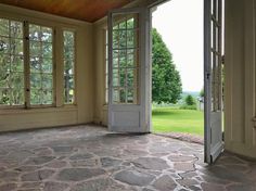 an empty room with stone floors and large windows looking out onto the green grass field