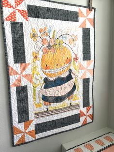 a quilt hanging on the wall next to a table with a potted plant in it