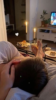 a person laying in bed with food on the table next to him and a candle