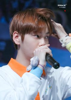 a young man holding a microphone up to his face while wearing an orange and white shirt