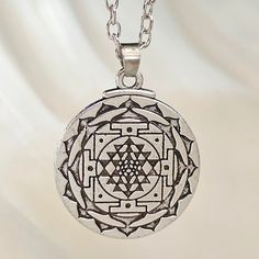 a silver necklace with an intricate design in the center on a white background that has a chain attached to it