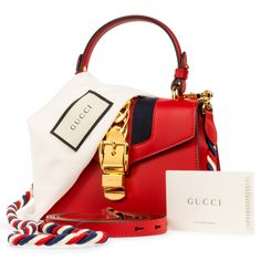 The Gucci Sylvie is one of those bags that became a classic the moment it landed in stores. The red hue is complimented by a white, blue and red woven fabric strap, ideal for cross-body usage - and if one strap wasn't enough, don't worry, you can find an additional red leather shoulder strap inside. This stunning bag is an absolute necessity, especially during holiday season. With a gold buckle chain prominently depicted on the front flap, the Sylvie is luxurious, glamorous and the perfect compl Red Shoulder Bag With Gold-tone Hardware For Everyday Use, Red Shoulder Bag With Adjustable Strap For On-the-go, Gucci Sylvie, Red Shoulder Bag With Gold-tone Hardware For Shopping, Red Shoulder Box Bag With Gold-tone Hardware, Red Shoulder Bag With Gold-tone Hardware And Double Handle, Monochromatic Outfit, Mini Shoulder Bag, Dior Shoes