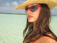 a woman wearing sunglasses and a straw hat standing in the shallow blue water on a sunny day