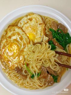 a white plate topped with noodles and meat next to chopsticks on a table